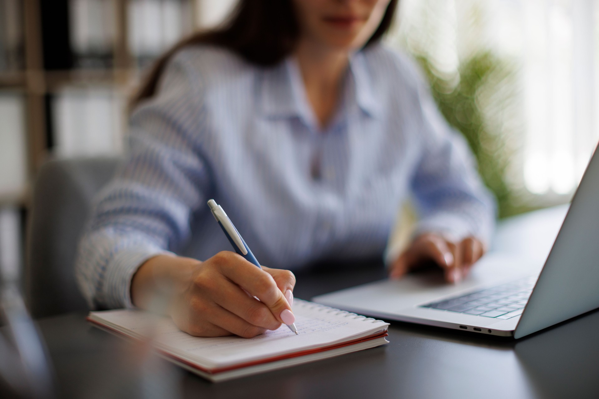Businesswoman taking notes in notebook while working on laptop in the office